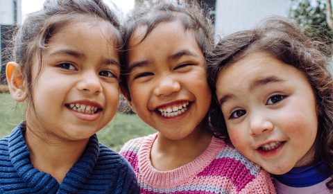 Three little girls in sweaters smiling outside.